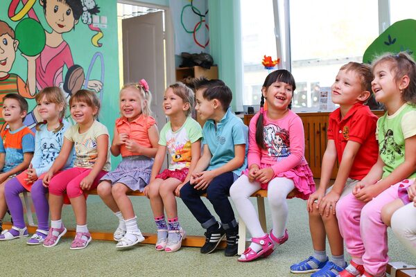 Neun Kinder sitzen auf einer Holzbank und lachen