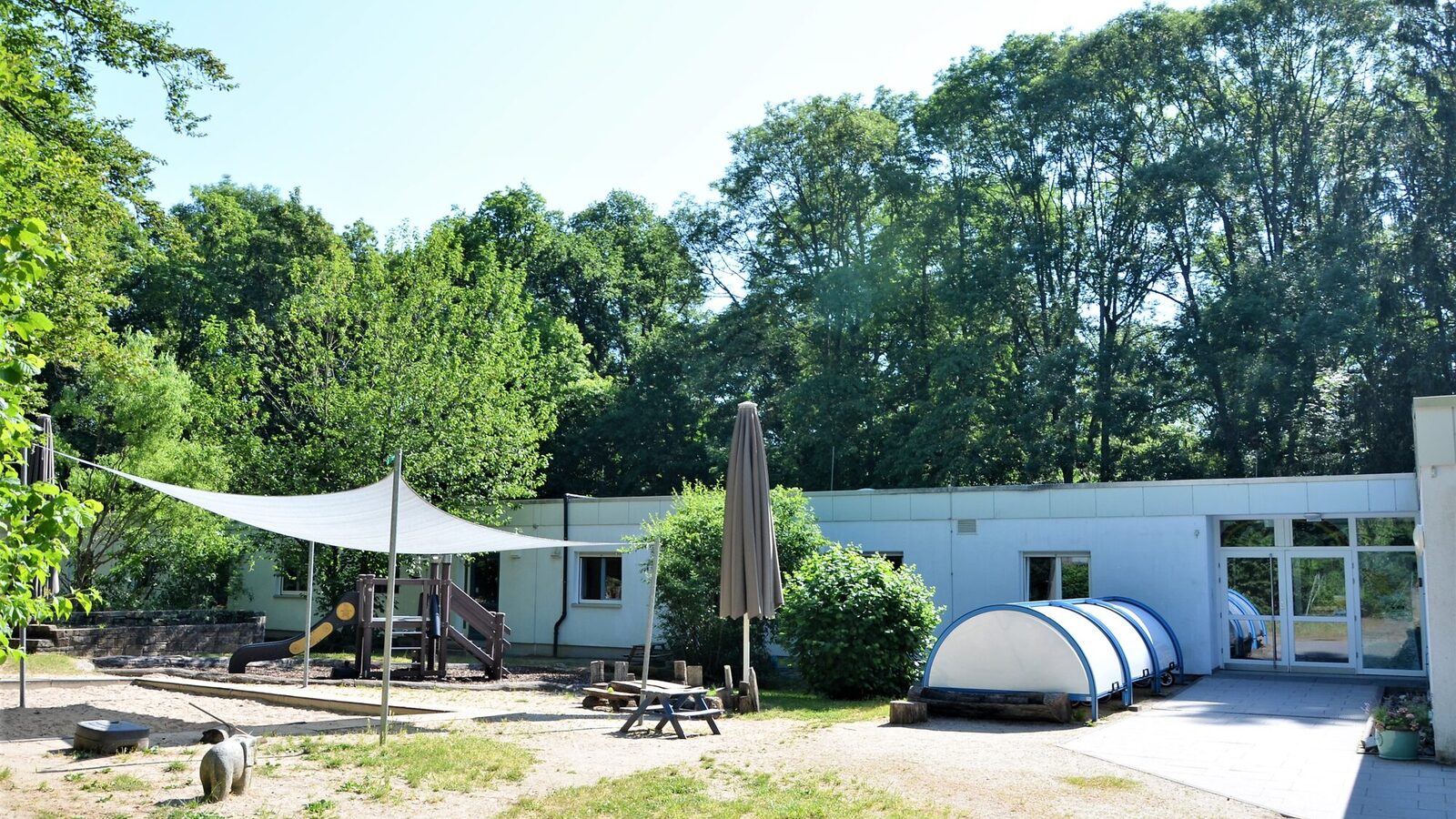 Der Sandspielplatz mit einem Sonnensegel - im Hintergrund das Gebäude