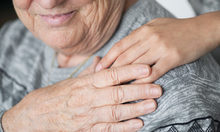 Helfende Hand auf Schulter einer sitzenden älteren Frau