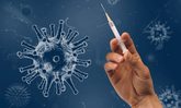 Corona-Impfungen: Hand mit Spritze vor Hintergrund symbolisierte Viren.