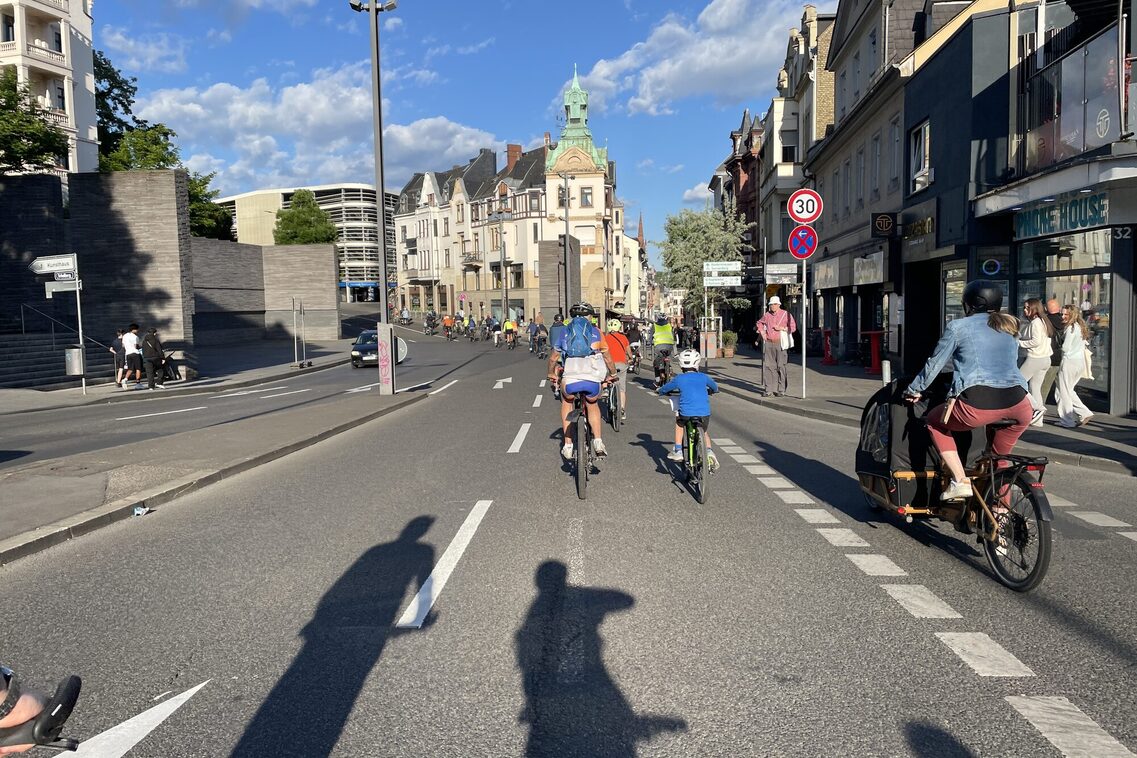 Große Gruppe Radfahrender, die bei Sonnenschein durch Wiesbaden fahren.