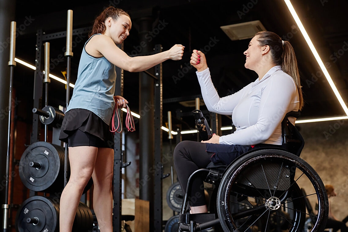 Zwei Frauen beim Sport, eine steht, die andere sitzt im Rollstuhl