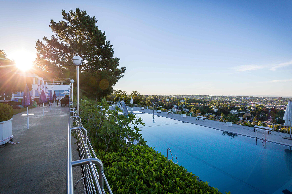 Ein Schwimmbad im Grünen hoch über einer Stadt gelegen.