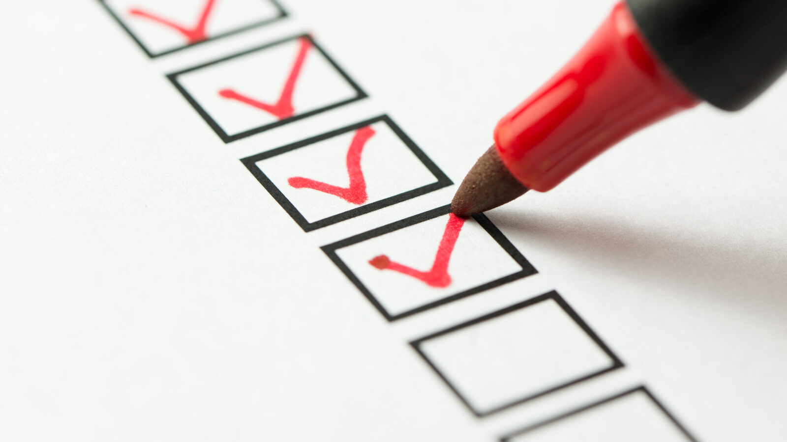 Sheet with six visible black boxes, three of which contain a red tick, pen tip sets another red tick.