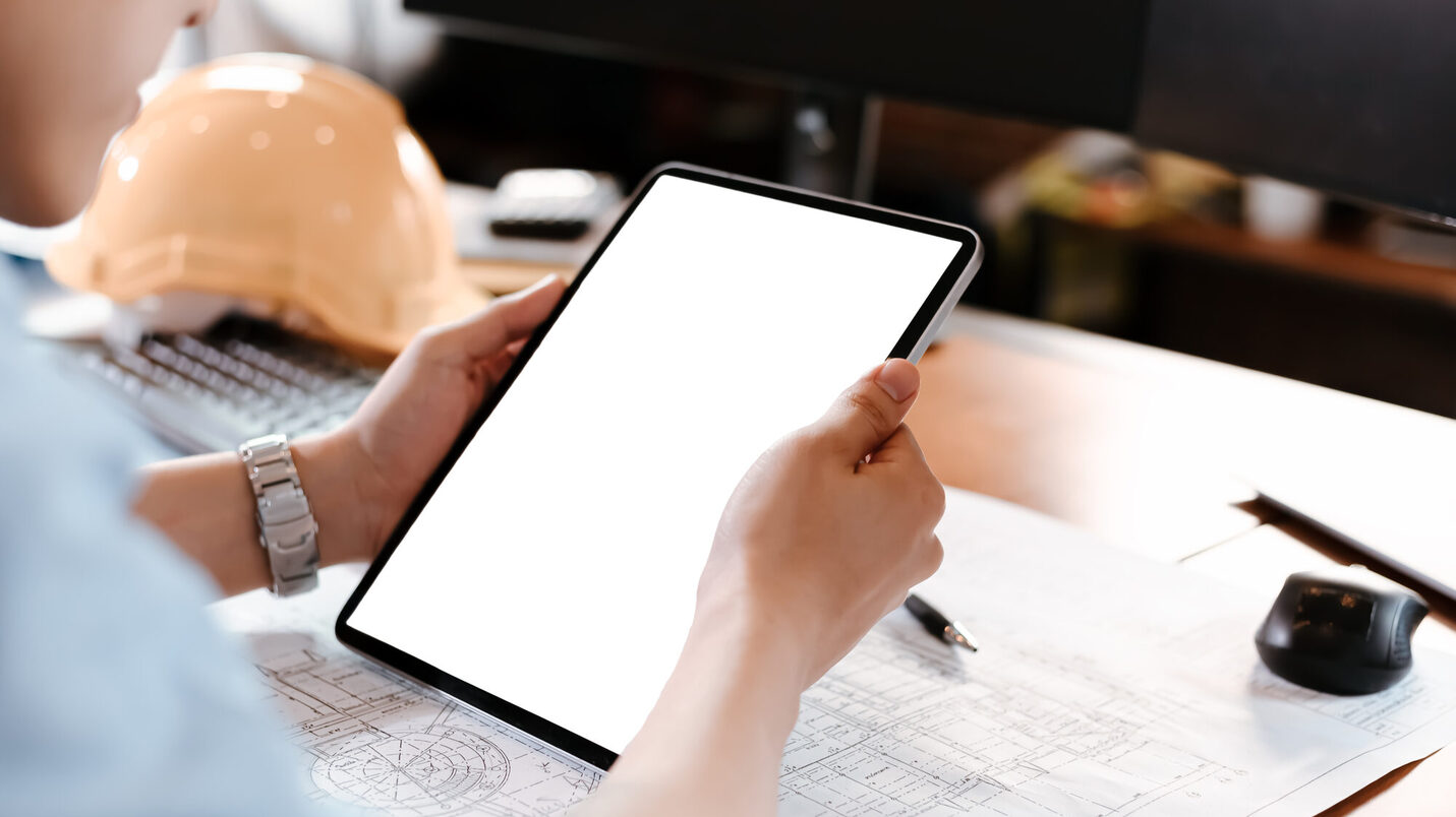 Architekt schaut auf ein Tablet und Baupläne