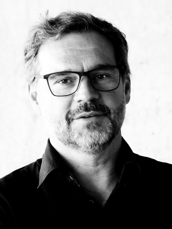 Das schwarz-weiß Bild zeigt das Portrait eines Mannes mit Brille und Bart. Sein Mund ist leicht geöffnet, der Kopf etwas nach hinten gelehnt, als setze er zum Sprechen an.