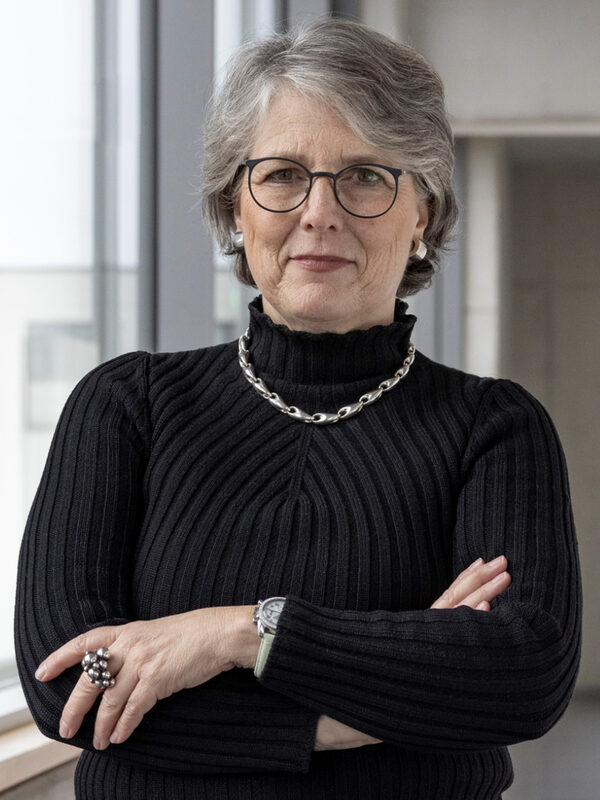 Eine Frau steht neben einem großen Fenster. Sie trägt eine Brille und lächelt.