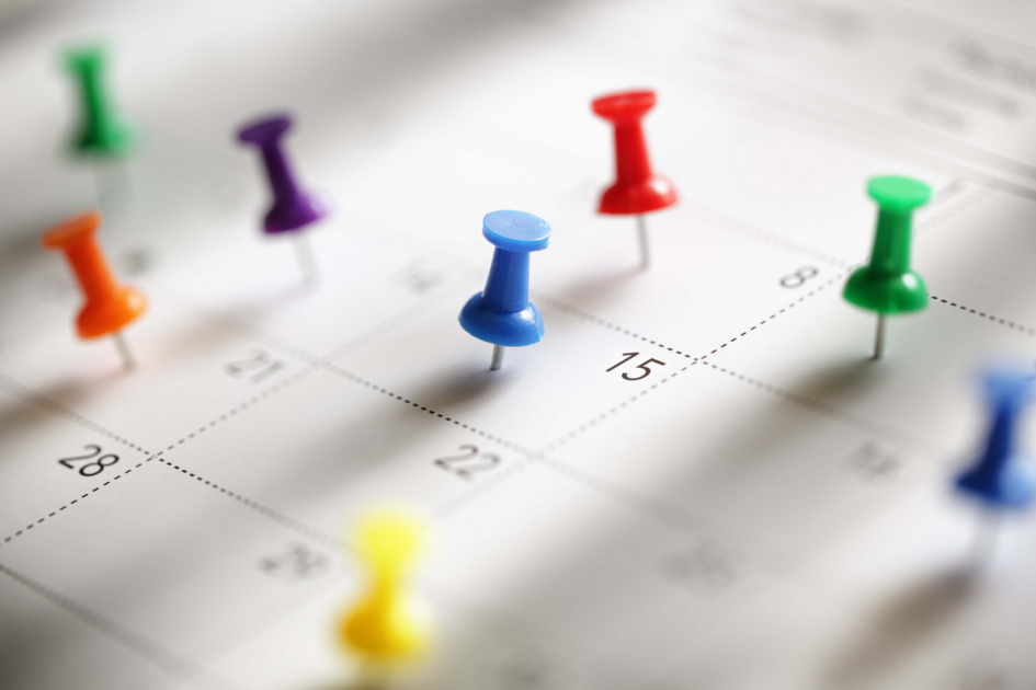 Nahaufnahme eines Monatskalenders mit bunten Pinnadeln auf einzelnen Tagen. Das Foto ist symbolischer Natur und kennzeichnet keine tatsächlich stattfindenen Veranstaltungstermine.