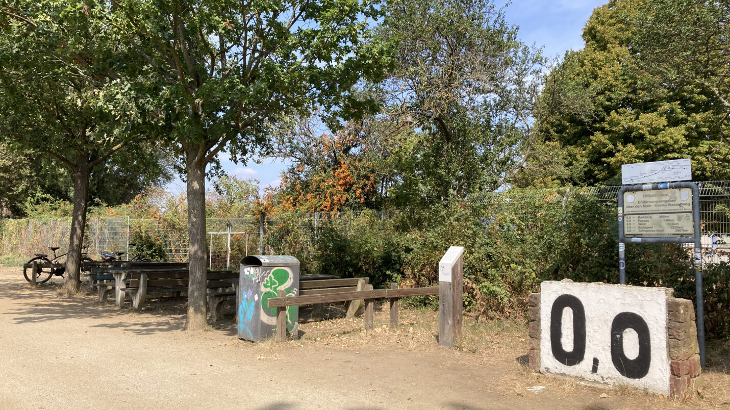 So sieht der Rastplatz am Mainkilometer heute aus – Tische und Bänke unter schattigen Bäumen.