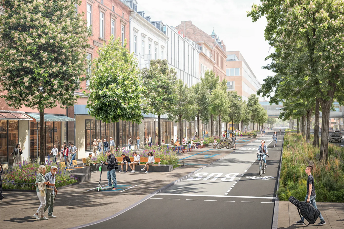 Diese Perspektive blickt auf die Ostseite der Schwalbacher Straße. Die Gehwege sind breiter, es gibt Aufenthaltsmöglichkeiten im Schatten der Bäume. Auf dieser Straßenseite gibt es nur noch Platz für eine Bus- und eine Radspur. Die Mittelinsel ist deutlich grüner und große Bäume wachsen in ihr.