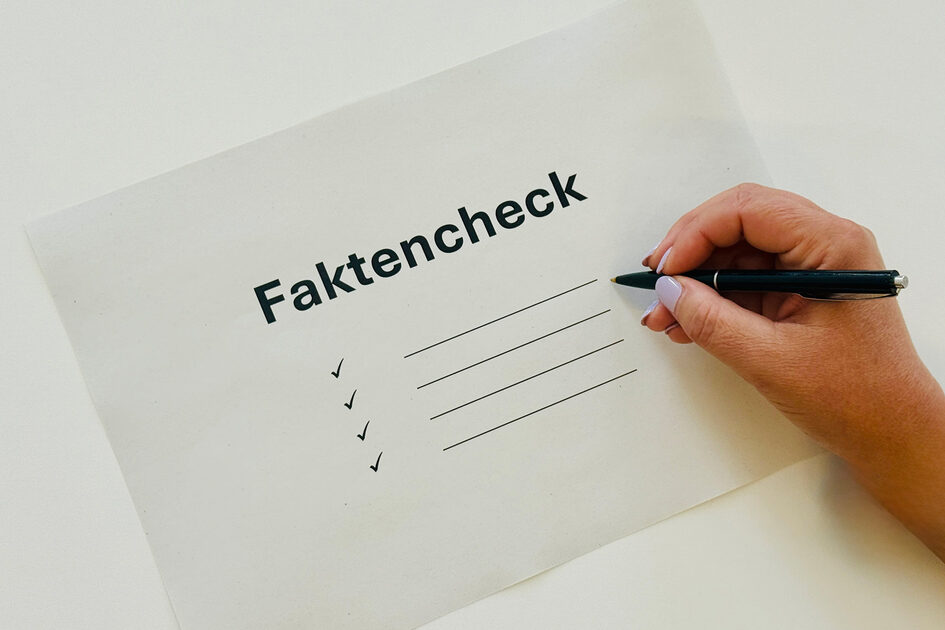 Hand mit Stift davor ein Papier mit der Aufschrift Faktencheck