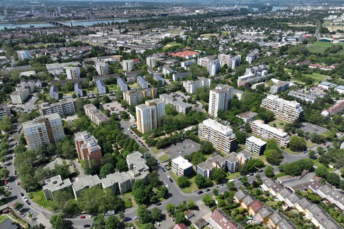 Luftbildaufnahme des Wohngebiets mit Hochhäusern, Zeilenbebauung und Reihenhäuser, im Hintergrund der Fluss Rhein