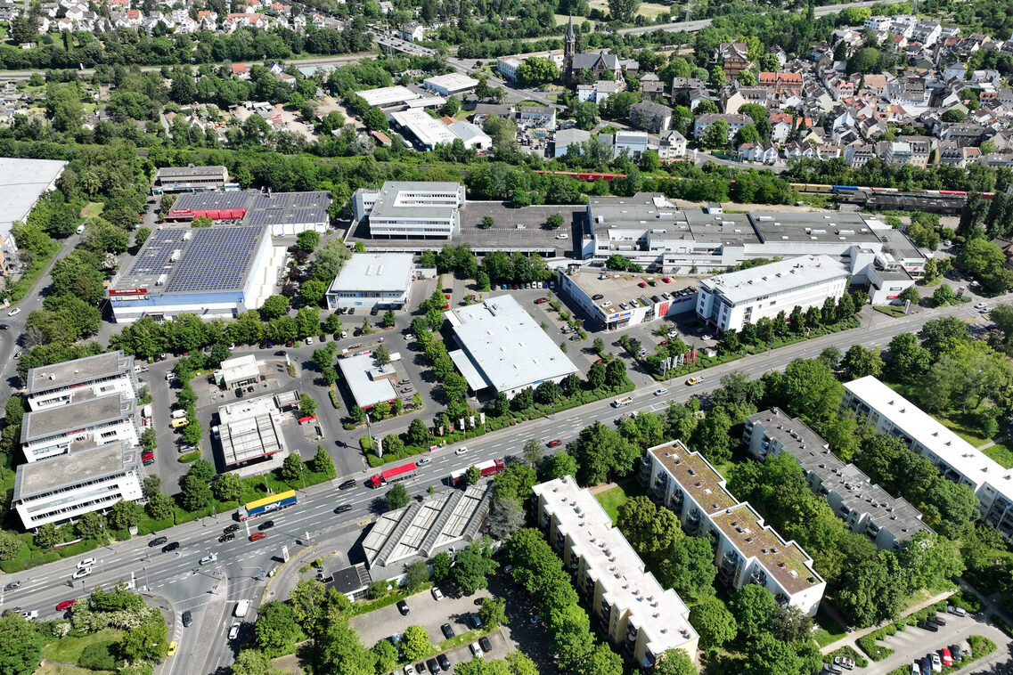 Hallen und Gebäude im Experimentierraum und dessen Umfeld. Die Äppelallee, Bundesautobahn A66 und die Bahntrasse werden mit Autos und Zügen befahren. Große Parkplätze werden durch einzelne Baumreihen begrenzt.