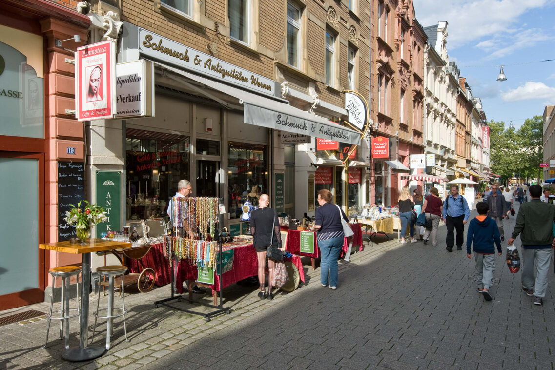 Menschen schlendern durch die Innenstadt, Läden stellen ihre Waren aus.