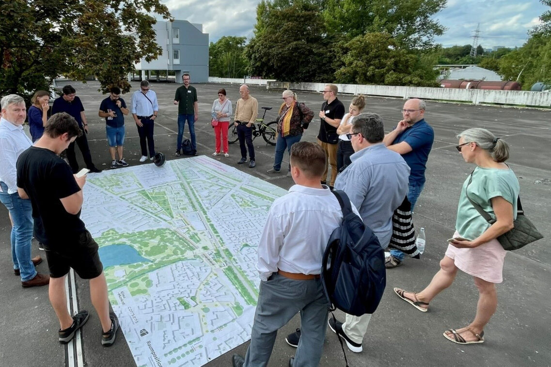 Eine Gruppe von Frauen und Männern steht um ein großes Plakat herum. Die Gruppe befindet sich auf einem leeren Parkdeck.