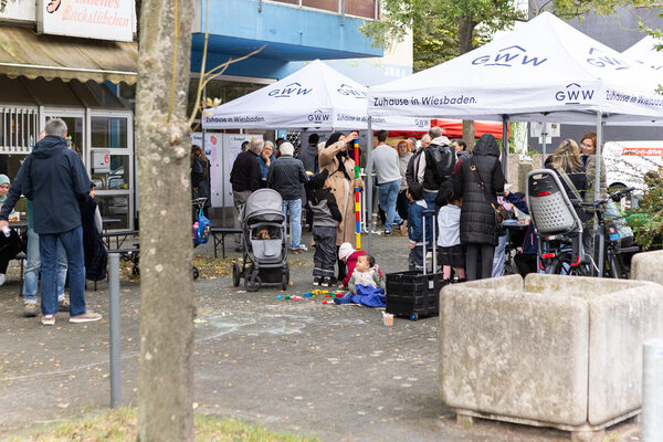 Many people stand under several pavilions in a square, gathering information and discussing with each other.