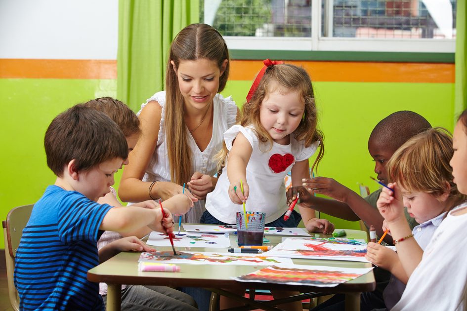 Zu sehen ist eine Frau und eine Gruppe Kleinkinder, die miteinander malen.