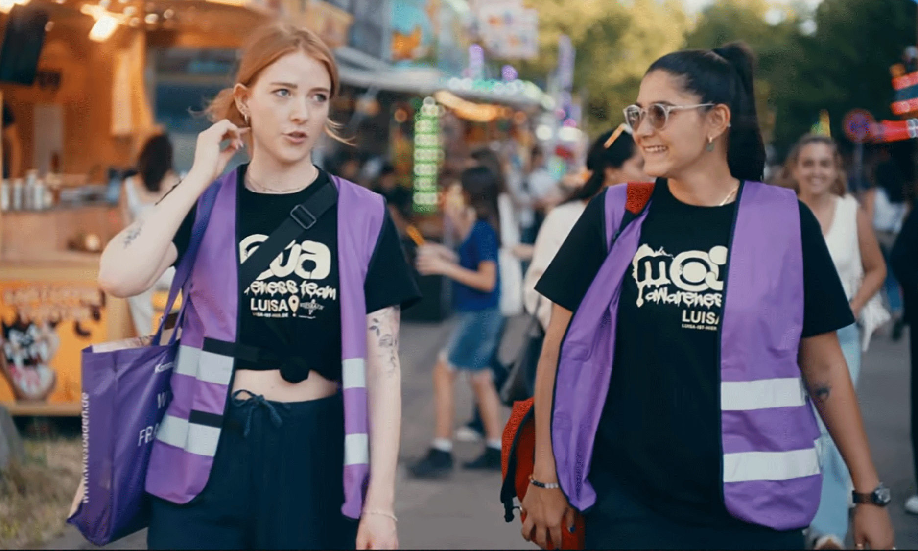 Aufklärungsvideo: Zwei Junge Frauen mit schwarzen Shirts und lila Weste.