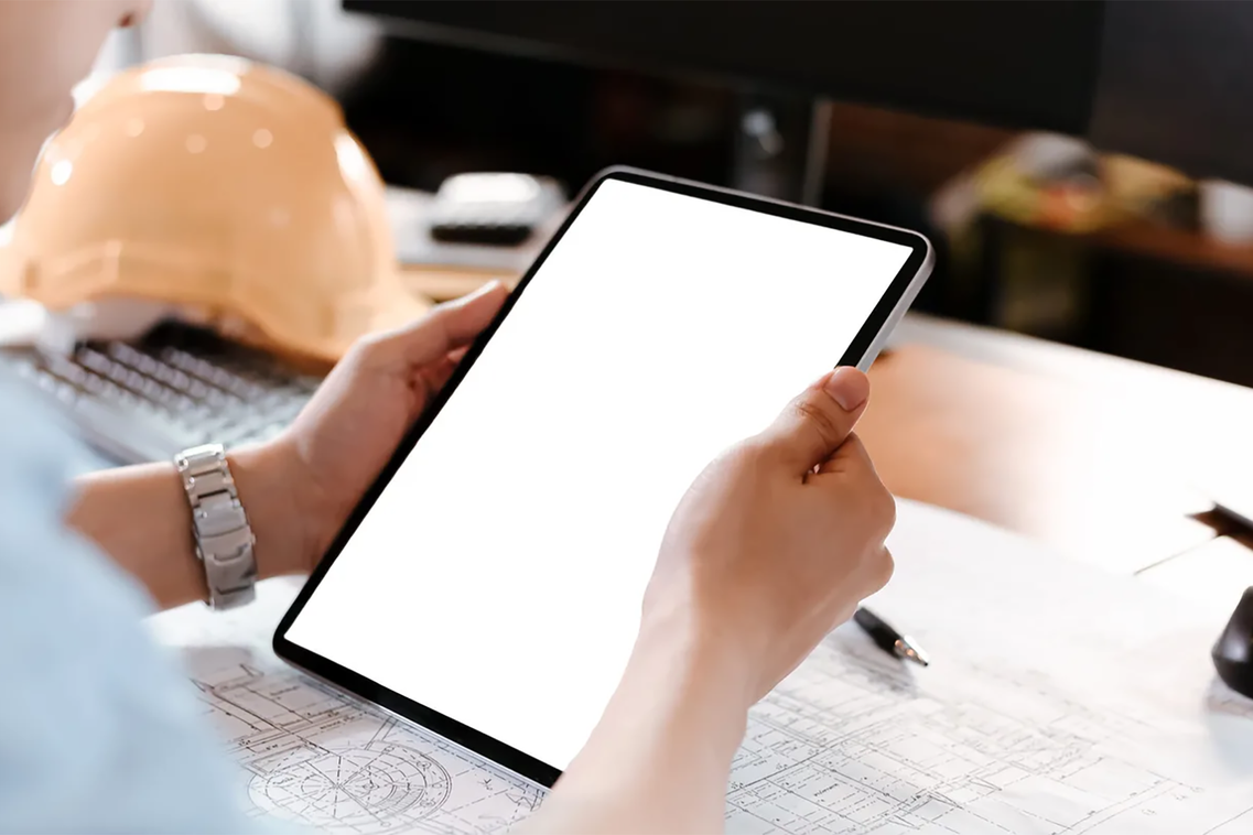 Architekt schaut auf ein Tablet und Baupläne