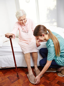 Pflegekraft hilft älterer Frau beim Aufstehen