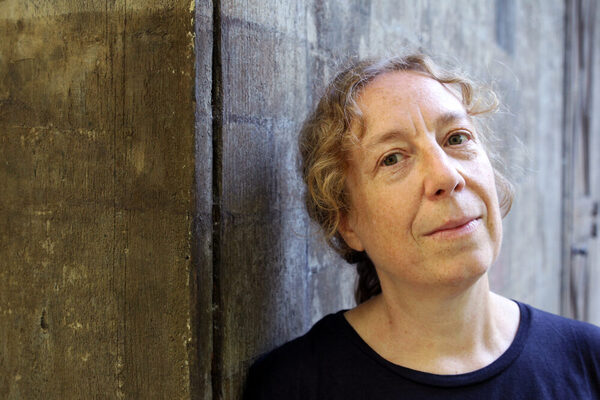 Donna davanti al muro con riccioli chiari e camicia blu.