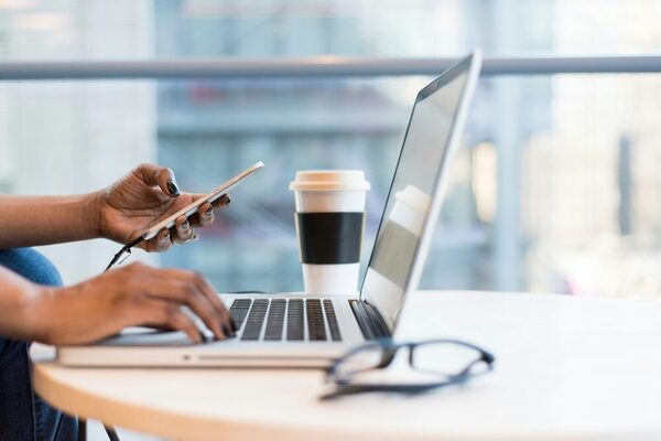 frauenhände-halten-ein-handy-und-tippen-in-einen-laptop