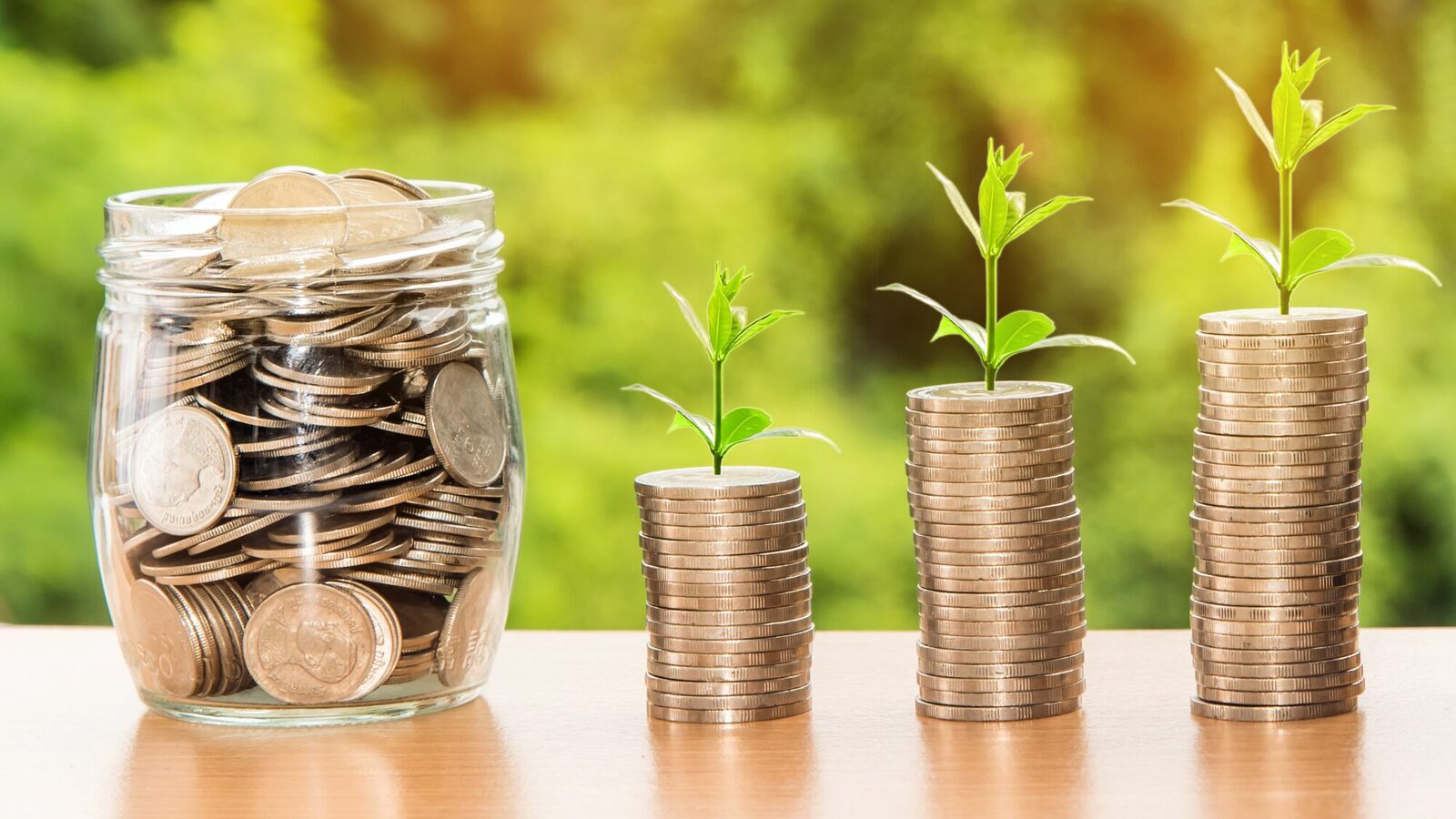 A jar with coins. Next to it, several coins are heaped in three towers from which plants are growing.