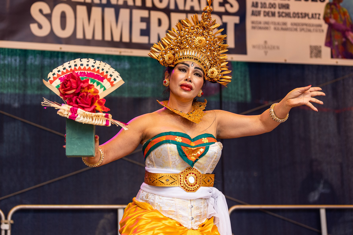 Жінка в костюмі стоїть на сцені з розпростертими руками.