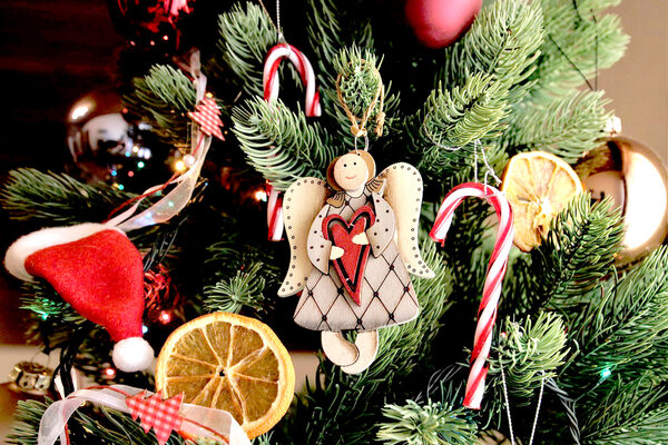 Zbliżenie na udekorowaną choinkę z cukierkami w biało-czerwone paski, drewnianym aniołem, suszonymi plastrami pomarańczy, małymi czapkami świątecznymi, złotymi i czerwonymi bombkami.