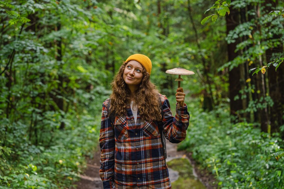 Frau steht im Wald und hält einen Pilz in der Hand