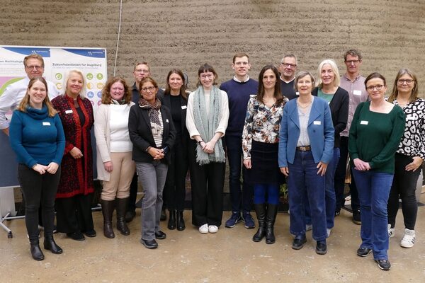 Grupa ludzi w różnych ubraniach stojących przed ścianą z dwoma plakatami.