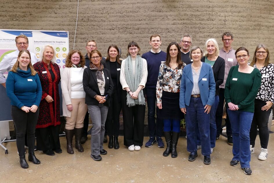 Gruppe von Menschen in unterschiedlicher Kleidung steht vor einer Wand mit zwei aufgestellten Plakaten.