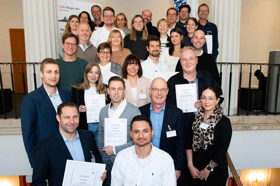 Mehrere Menschen stehen hintereinander. Manche halten Urkunden in ihren Händen. Viele lächeln.