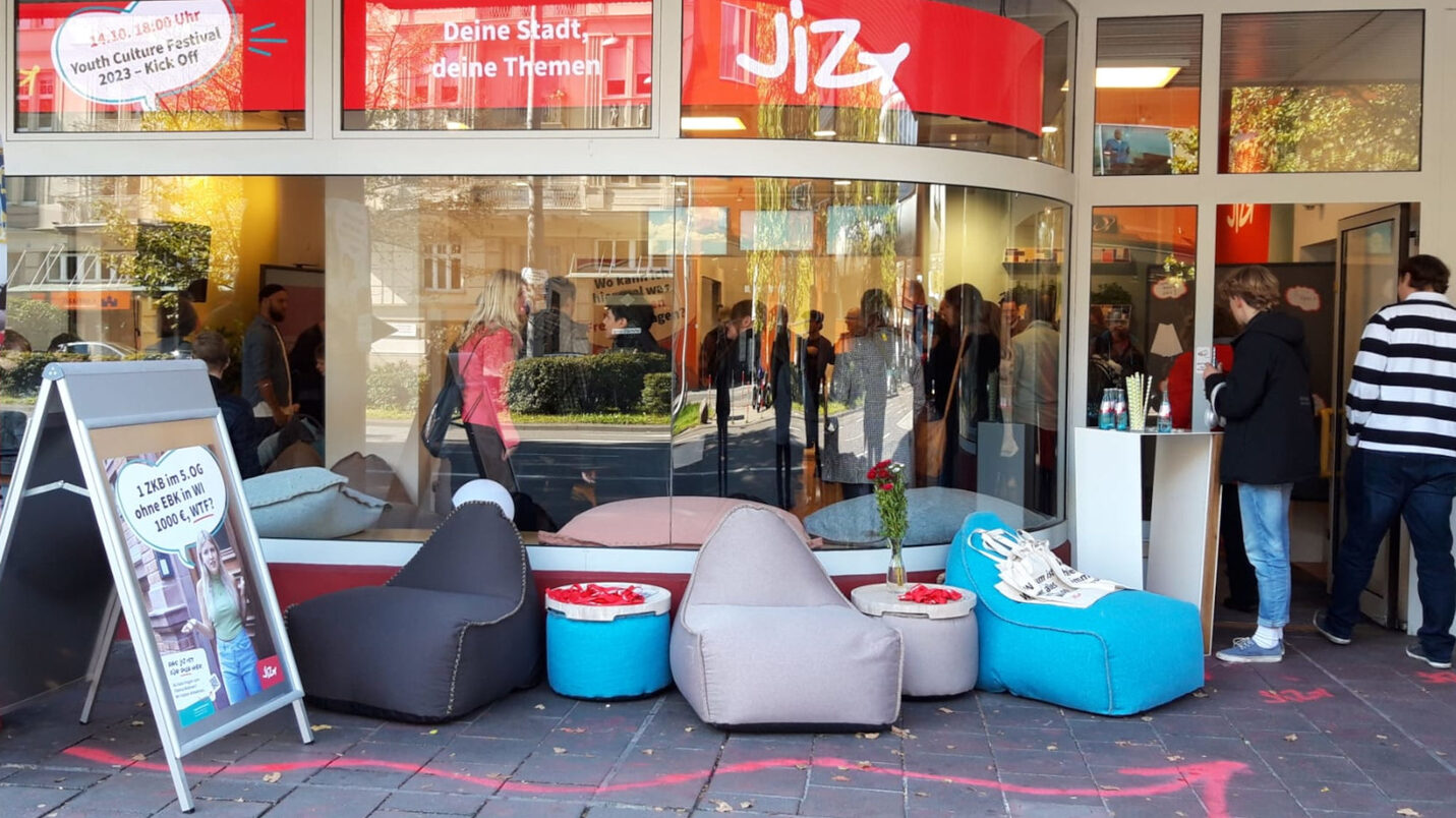 Vor einem Schaufenster stehen blaue, graue und schwarze Sitzsäcke. Oben steht auf einem Schriftband "JIZ".