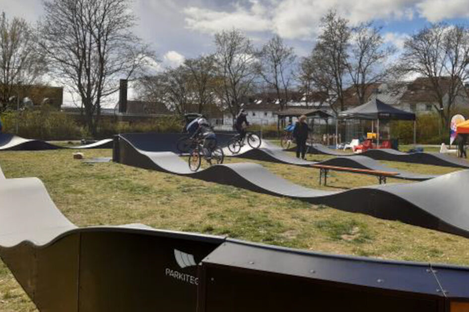 Auf einer Wiese sind Pumptracks zu sehen, gewellte Bahnen, auf denen man mit Fahrrädern fahren kann.
