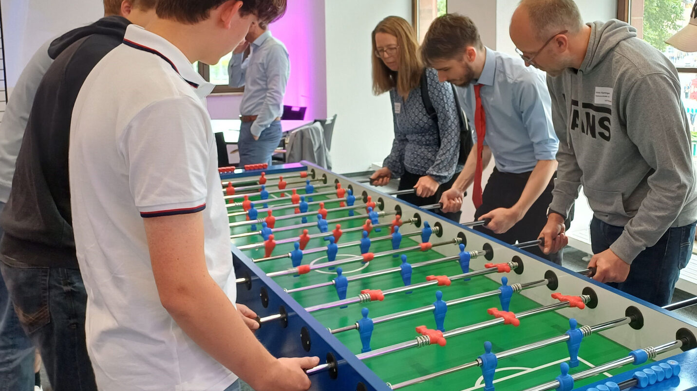 Jugendliche und Erwachsene stehen an einem Tischkicker.