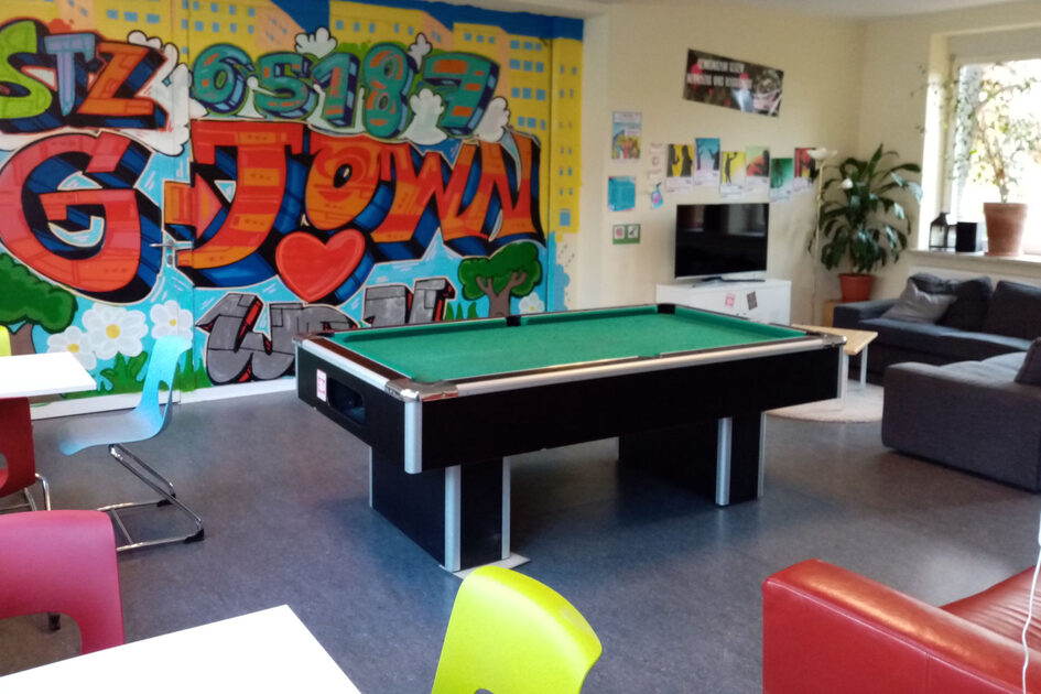 Ein Raum mit bunten Sesseln, einer Wand mit Graffiti und einem Kickertisch.