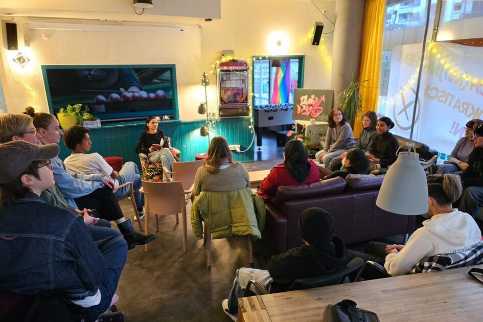 Mehrere Menschen sitzen zusammen auf Sofas und Stühlen.