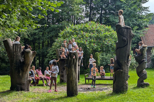 Children sit on tree trunks and a meadow.
