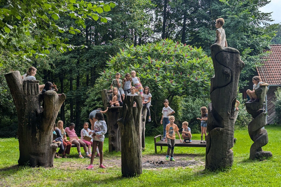 Kinder sitzen auf Baumstämmen und einer Wiese.