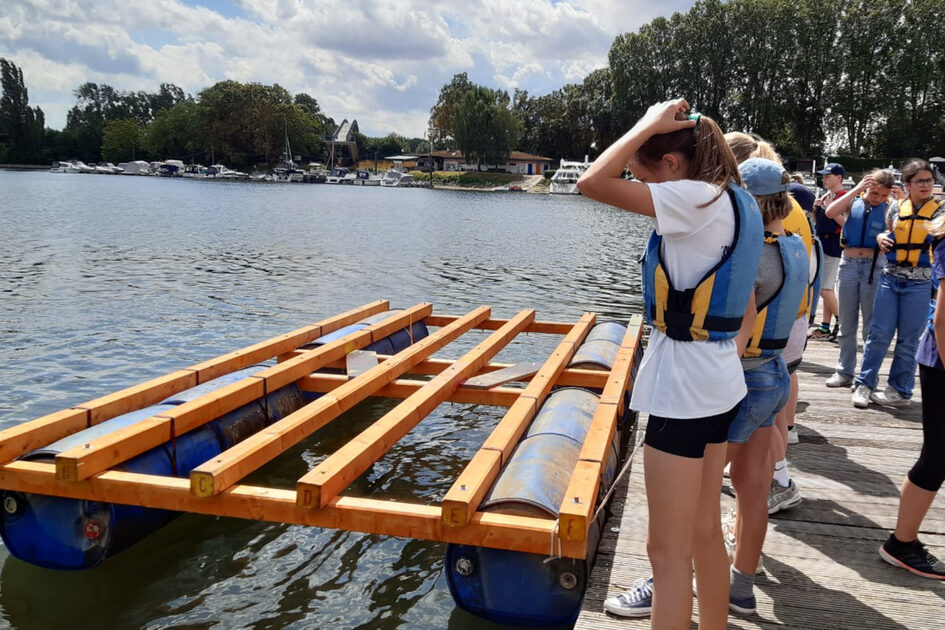 Mädchen mit Schwimmwesten stehen an einem Anleger am Wasser.