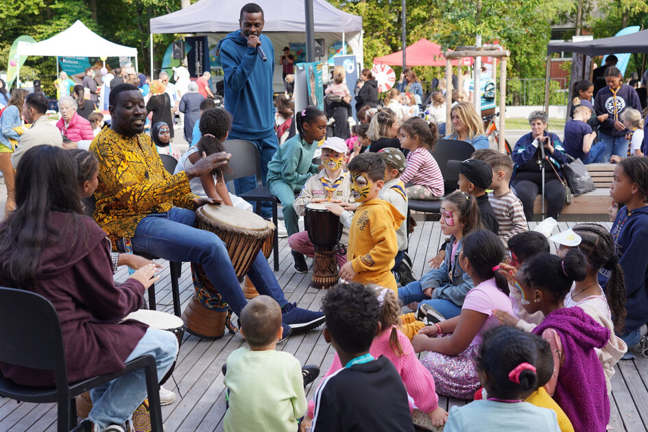 Kinder und Frauen sitzen auf dem Boden, zwei afrikanische Männer machen Musik, sie trommeln und singen.