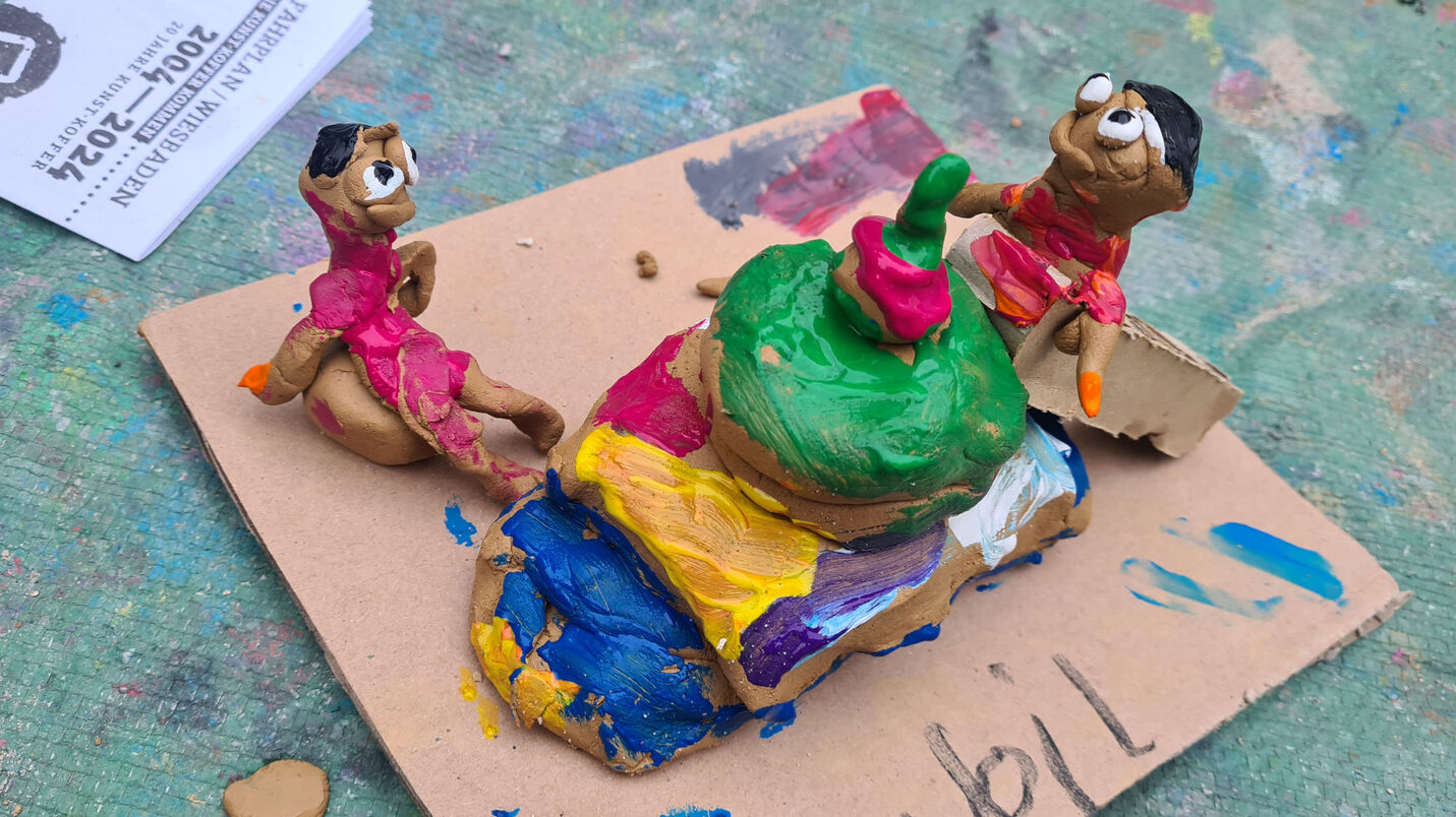 Auf einer Pappe sitzen zwei bemalte Knetfiguren.