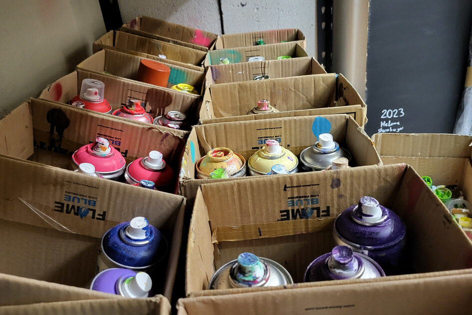Bunte Spraydosen stehen in Pappkartons.