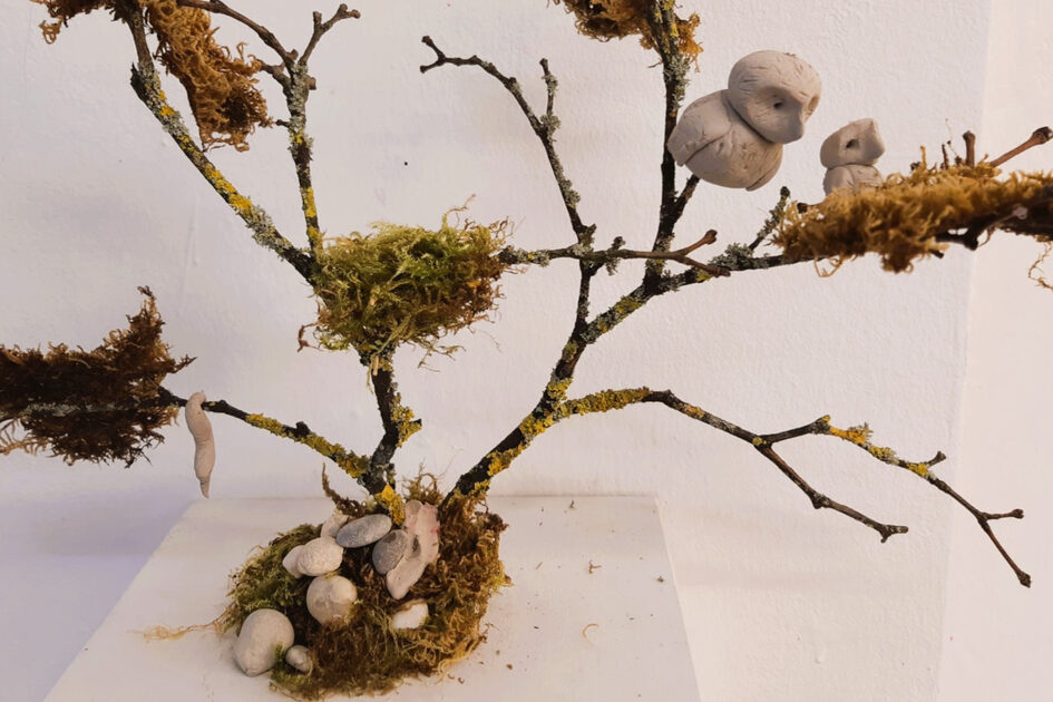 Äste sind mit Moos bedeckte und sind zu einem Baum drapiert. Tontiere, wie Eule und Wurm sitzen auf den Ästen.
