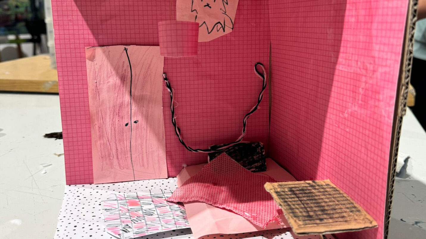 يمكنك أن ترى نموذجًا من الورق المقوى لغرفة، جدرانها وردية اللون وأرضيتها منقطة ومن الواضح أنها من صنع طفل.