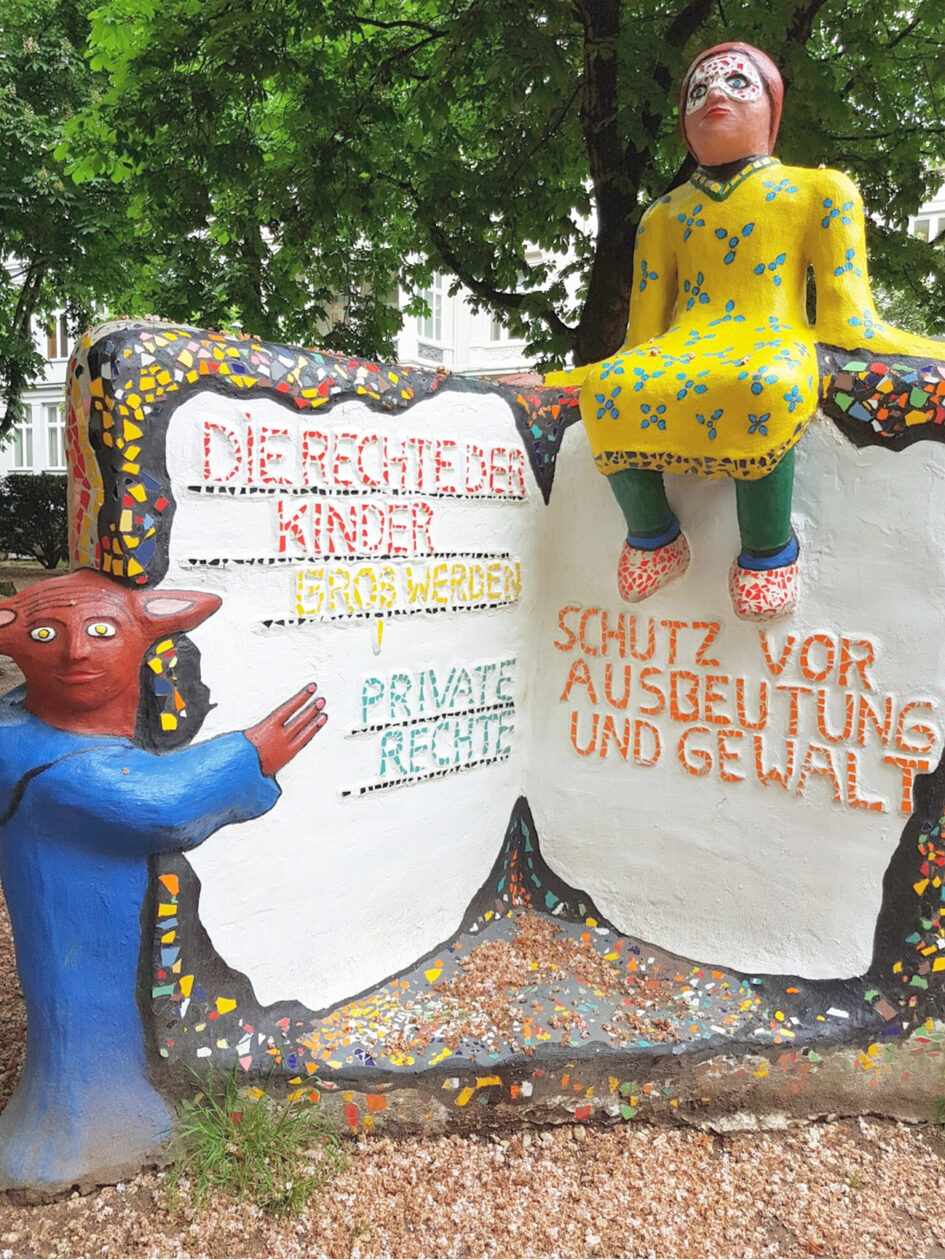 Ein Denkmal zeigt ein aufgeklapptes Buch mit Rechten der Kinder, zwei Figuren sind dazu angeordnet.