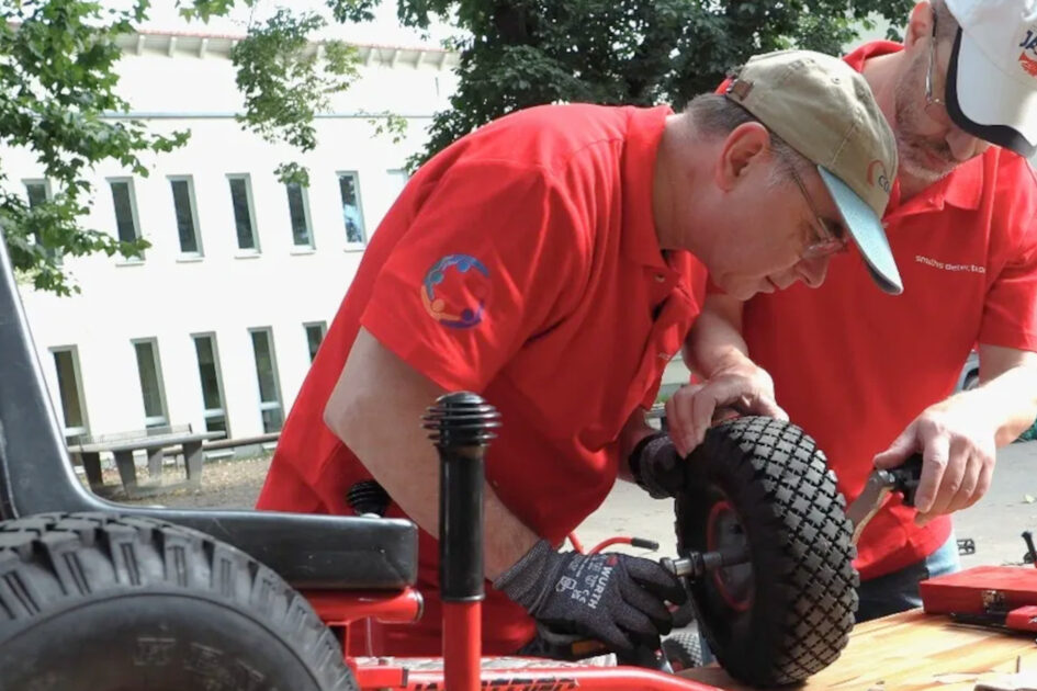 Zwei Männer in roten T-Shirts reparieren einen kleinen Reifen.