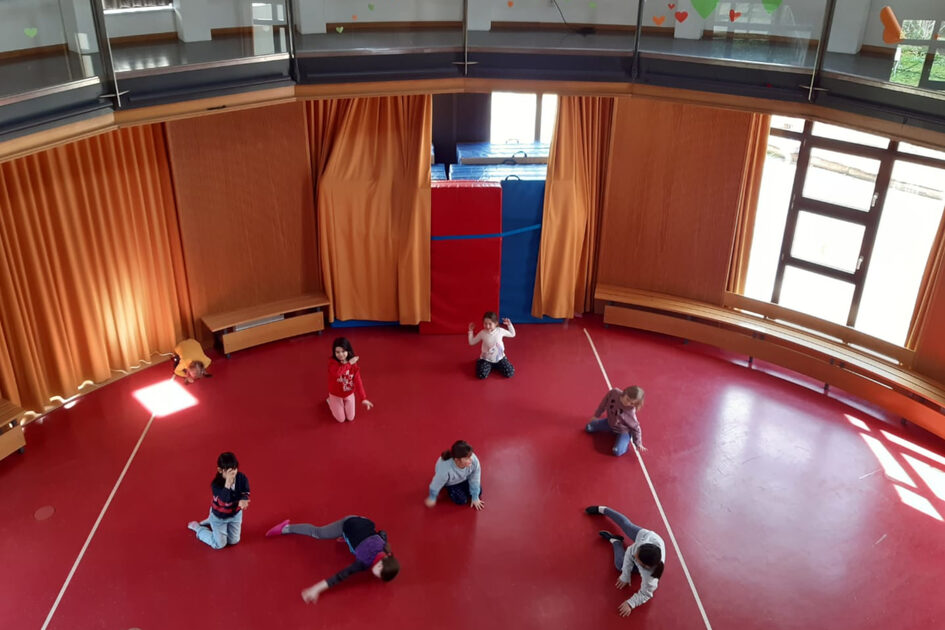 In einer runden Turnhalle mit rotem Boden machen Kinder Turnübungen.