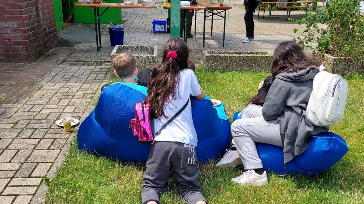 Drei Jugendliche liegen und sitzen auf Sitzsäcken vor einem Eingangsbereich.